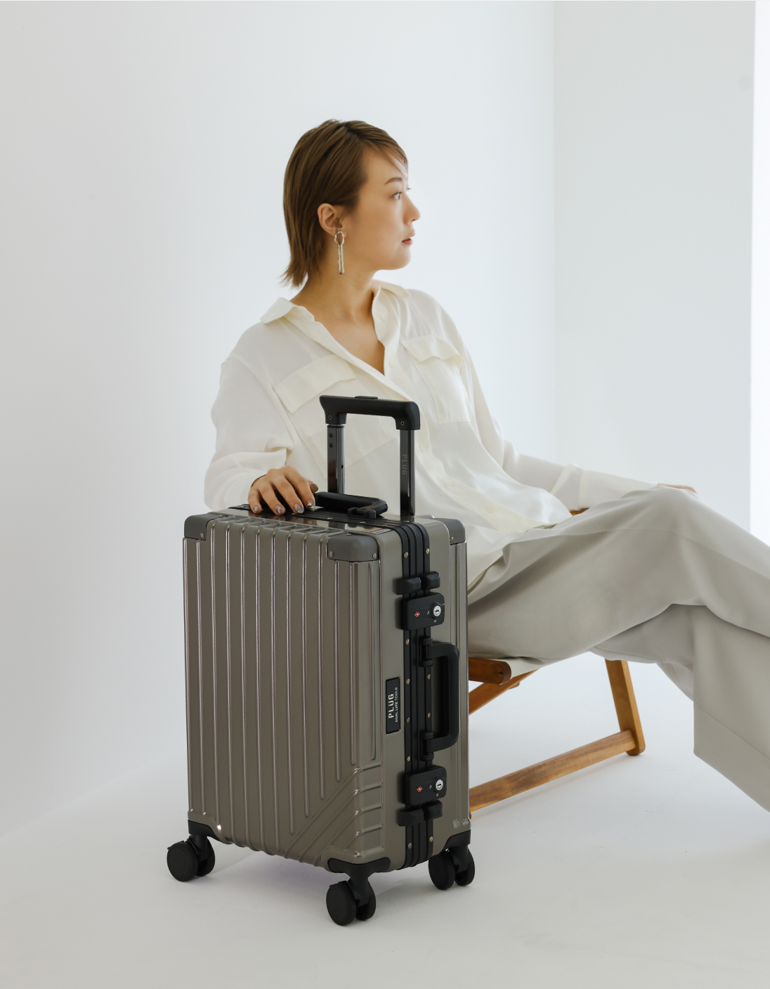 ウッドと帆布のオシャレなチェアに座り、スーツケースに手をかけている女性モデル